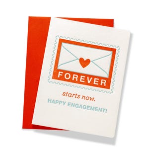 Op de afbeelding: Een witte verlovingskaart met een rode envelop. De kaart heeft een postzegelontwerp met een envelop- en hartillustratie. Het woord "FOREVER" staat boven de zin "starts now." en "HAPPY ENGAGEMENT!"