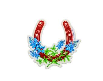 以下が含まれることがあります： 赤い馬蹄形のステッカーに、青と緑のテキサスブルーボンネットの花が描かれています。ステッカーには「color box happiness」と書いてあります。