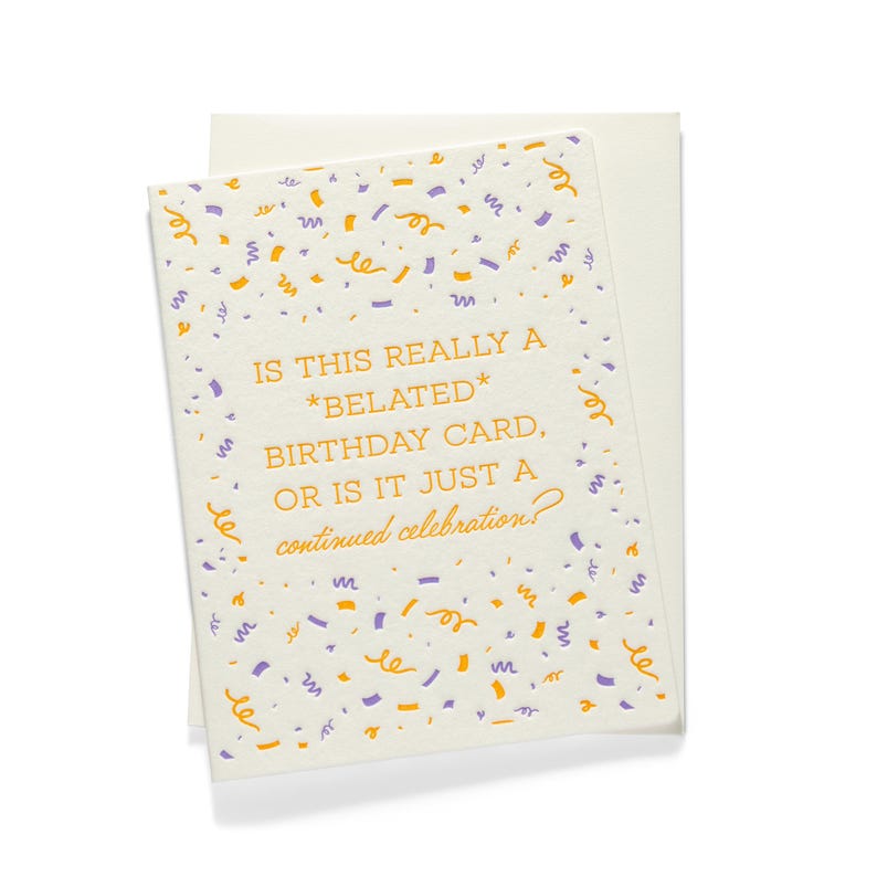 Puede incluir: Una tarjeta de cumplea&ntilde;os color crema con un sobre a juego. La tarjeta presenta confeti morado y naranja y el texto: "IS THIS REALLY A *BELATED* BIRTHDAY CARD, OR IS IT JUST A continued celebration?"