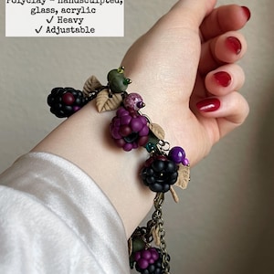 May include: A hand-sculpted bracelet with brass and copper alloy chains, polyclay blackberries, and glass beads. The bracelet is 22.86 cm long and has a heavy feel. The design includes adjustable features.