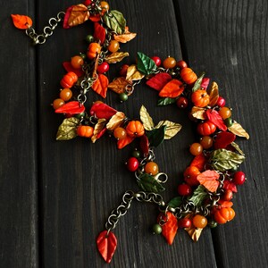 May include: A fall-themed necklace with orange, red, and gold leaves, small orange pumpkins, and brown beads. The necklace is made of metal chain and polymer clay.