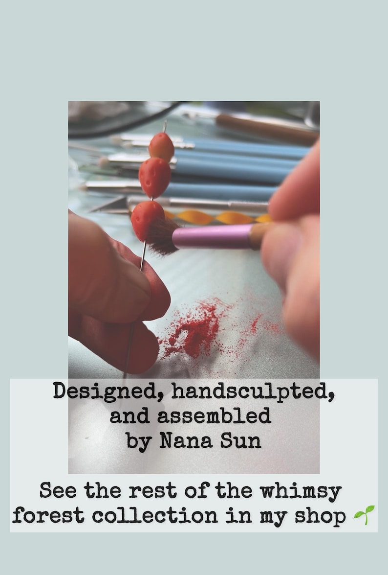 May include: A craft project in progress is shown. Three small, red, berry-like objects are impaled on a needle. A pink brush is used to apply a red powder. Text reads: Designed, handsculpted, and assembled by Nana Sun.