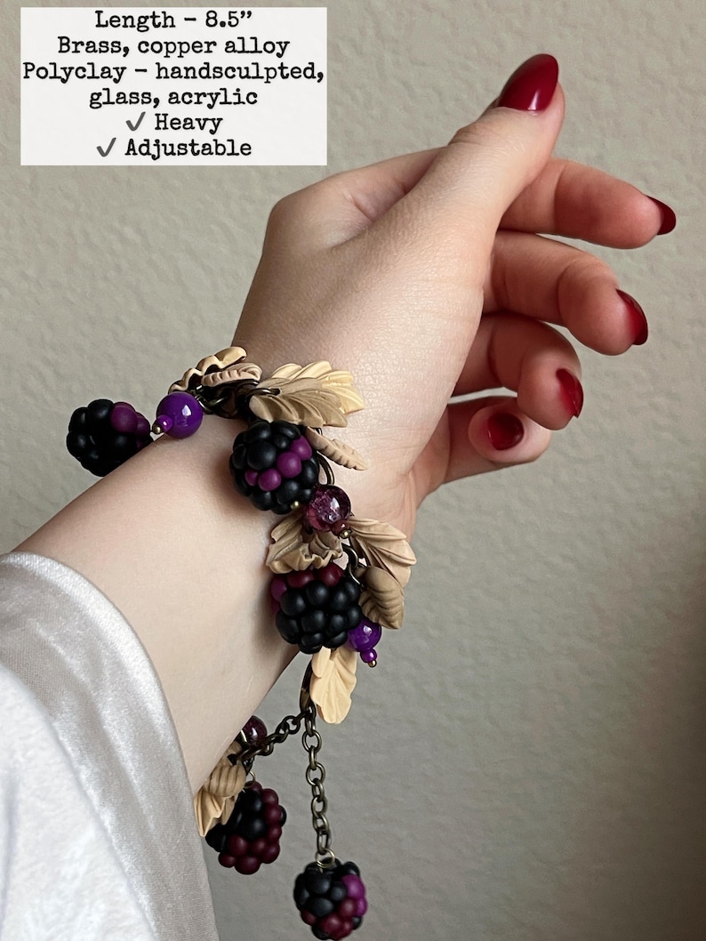 May include: A hand-sculpted bracelet with brass and copper alloy elements, polyclay, glass, and acrylic. It features black and purple berry clusters, beige leaves, and purple beads. The bracelet is 21.6 cm long, heavy, and adjustable.