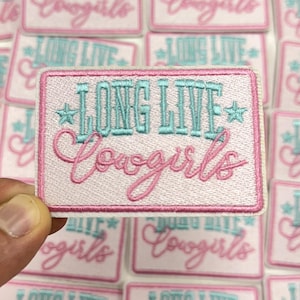 May include: A rectangular patch with the text "LONG LIVE Cowgirls" in turquoise and pink embroidery. The patch has a white background with a pink border and star accents. Multiple patches are visible in the background.
