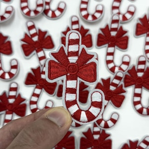 May include: Embroidered candy cane patches with red bows and white and red striped candy canes. The patches are a festive holiday decoration.