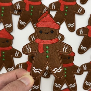 May include: Brown gingerbread man patch with a red hat and scarf, and white stitched details. The patch has a smiling face and green button details. Several patches are visible.