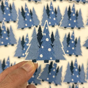 May include: Embroidered patches featuring a stylized blue Christmas tree design with white polka dots. The patches are in various shades of blue and are arranged on a white background. The patches are suitable for clothing or craft projects.