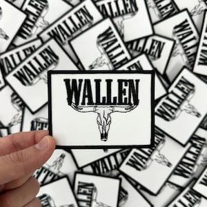 May include: A rectangular white patch with the word "WALLEN" in bold black letters above a black bull skull design. The patch is surrounded by a black border. Other similar patches are in the background.