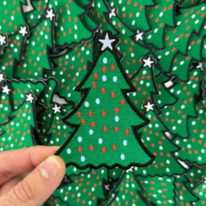 May include: A green felt Christmas tree patch with red, white, and blue ornaments. The tree has a white star on top and a black outline.