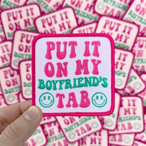 May include: Pink and green embroidered iron-on patch with the text "Put it on my boyfriend's tab" and two smiley faces.