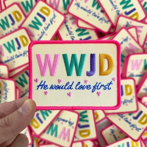 May include: A stack of colorful embroidered iron-on patches with the text "WWJD He would love first".