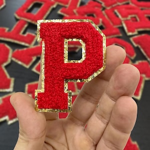 May include: Red felt letter P with a gold glitter outline. The letter is held in a hand.