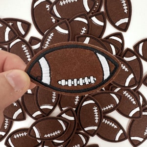 May include: A pile of brown felt football patches with white stitching. The patches are approximately 3 inches long and 1.5 inches wide.
