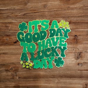 May include: Green glitter letters spelling "It's a good day to have a lucky day" on a wood background.