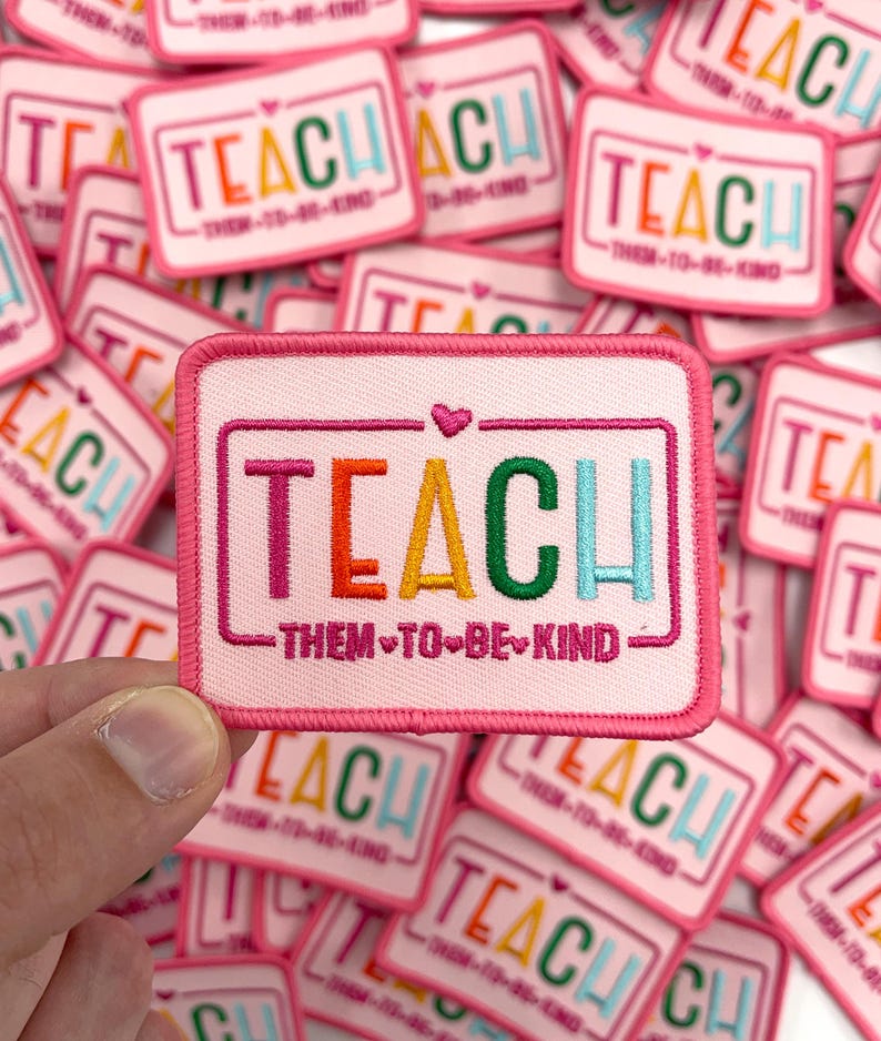 a hand holding a patch that says teach them to be kind
