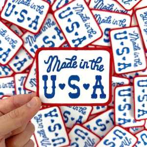 May include: Rectangular white patch with a red border and the text "Made in the USA" in blue script. The letters "U.S.A" are also in blue, with hearts between the letters. Multiple patches are visible.