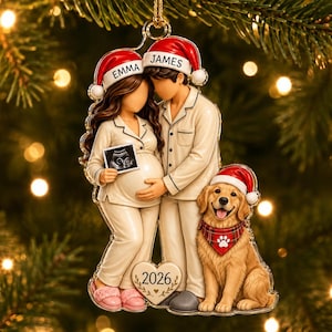 Puede incluir: Un adorno navideño con una pareja en pijama color crema y un golden retriever con gorro de Papá Noel rojo y pañuelo a cuadros. La pareja lleva gorros con los nombres EMMA y JAMES, sosteniendo una ecografía. Un corazón en la base indica 2026.