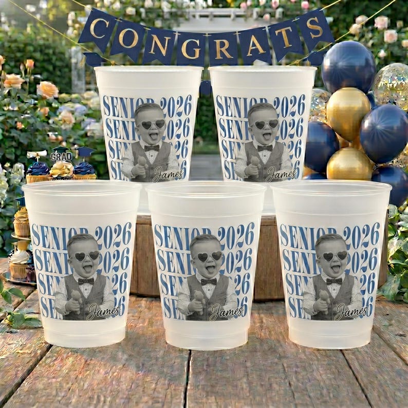 K&ouml;nnte beinhalten: Sechs wei&szlig;e Plastikbecher mit dem Aufdruck "SENIOR 2026" in Blau und einem Schwarz-Wei&szlig;-Bild eines Babys mit Sonnenbrille und Fliege. Die Becher sind mit dem Namen "James" personalisiert.