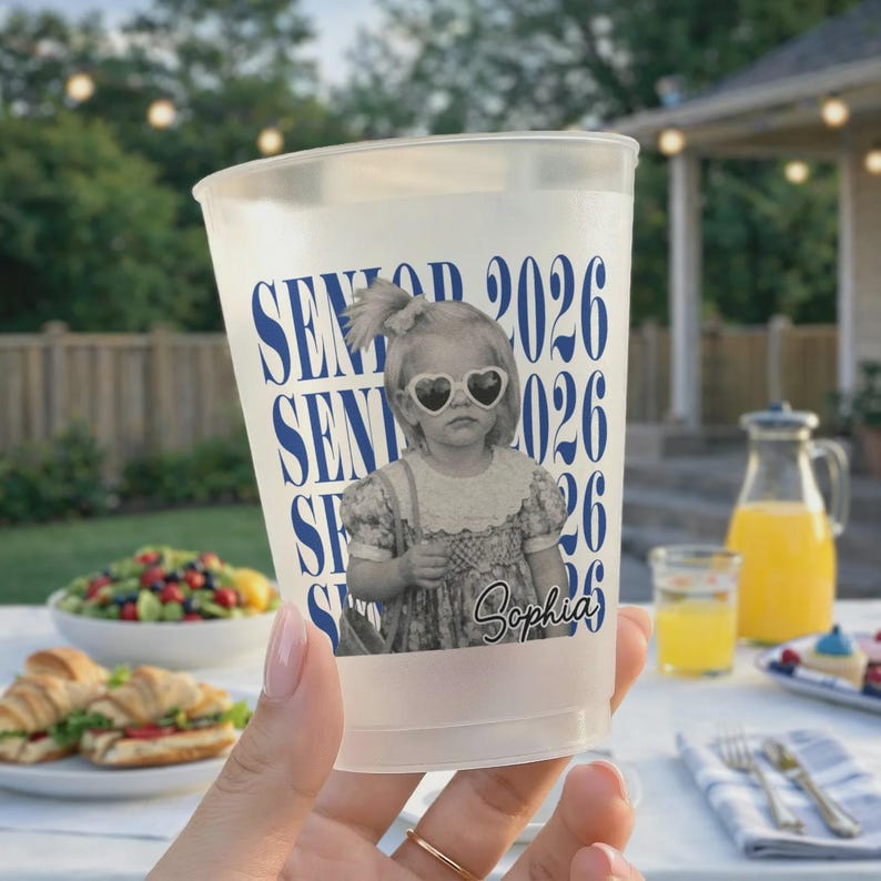 K&ouml;nnte beinhalten: Ein durchsichtiger Plastikbecher mit den Worten "SENIOR 2026" in Blau. Der Becher zeigt ein Schwarz-Wei&szlig;-Bild eines jungen M&auml;dchens mit herzf&ouml;rmiger Sonnenbrille. Der Name "Sophia" steht darunter.