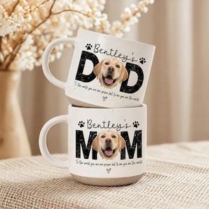 May include: Two white ceramic mugs stacked on top of each other. The top mug says "Bentley's Dad" with a photo of a yellow Labrador. The bottom mug says "Bentley's Mom" with a similar photo. Both mugs have a paw print design.