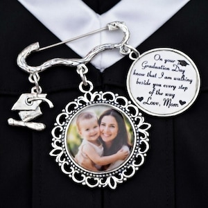 May include: A silver graduation pin with a photo pendant and a mortarboard charm. The photo pendant features a mother and child. A circular pendant reads "On your Graduation Day...Love, Mom."