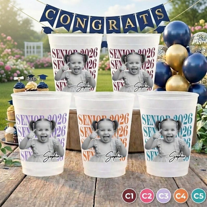 K&ouml;nnte beinhalten: Transparente Plastikbecher mit einem Foto eines Kindes, dem Text "SENIOR 2026" und dem Namen "Sophia". Ein Banner dar&uuml;ber lautet "CONGRATS". Luftballons und Cupcakes im Hintergrund. Abschlussfeier-Zubeh&ouml;r.