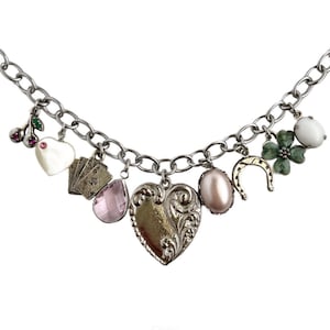May include: A silver charm bracelet with a variety of charms, including a heart, a horseshoe, a four-leaf clover, a playing card, a cherry, and a pearl.
