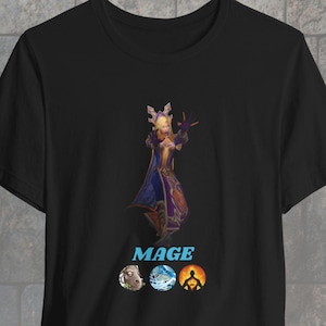 May include: Black t-shirt with a graphic of a female mage character with blonde hair and a purple and blue robe. The text "MAGE" is below the character, and three icons are below the text. The icons are a sheep, a wave, and a person with a sun behind them.