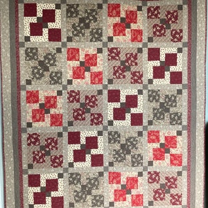 May include: A quilt with a patchwork design featuring squares of red, white, and brown fabric. The quilt is made up of a grid of squares, each with a different pattern. The quilt is framed with a brown border.