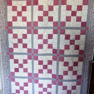May include: A quilt with a patchwork design featuring alternating squares of white and pink fabric. The quilt is bordered with a floral print fabric.