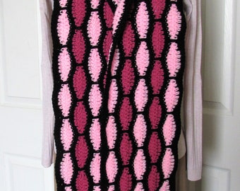 May include: A long crocheted scarf with a black, pink, and burgundy pattern. The scarf is made with a repeating pattern of oval shapes.