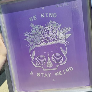 May include: A purple screen printing frame with a white design that says "Be Kind & Stay Weird" with a skull and floral design.