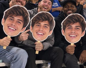 May include: Three identical handheld cardboard cutouts featuring a high-resolution colour photograph of a smiling young person with brown hair. Each cutout is mounted on a flat wooden stick, designed for display at events or gatherings.