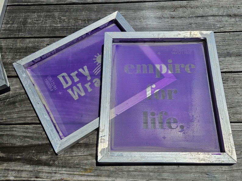 May include: Two purple screen printing frames with silver frames. The left frame has the text "Dry Wrap" printed on it. The right frame has the text "empire for life" printed on it.