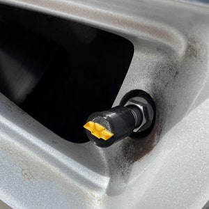 Puede incluir: Primer plano de una válvula de neumático con una tapa de válvula amarilla. El neumático está montado en una llanta plateada y tiene la palabra "OUTSIDE" impresa en la pared lateral.