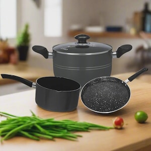 Könnte beinhalten: Ein Set schwarzer Kochutensilien, darunter ein Topf mit Glasdeckel, ein Kochtopf und eine gesprenkelte Bratpfanne. Das Kochgeschirr wird auf einer Holzoberfläche mit grünen Bohnen, einer kleinen roten Frucht und einer Limette präsentiert.