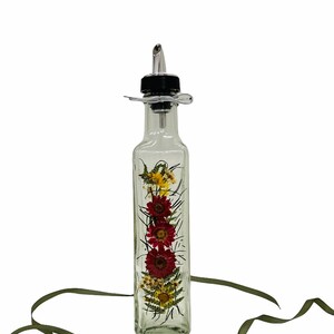 Puede incluir: Una botella de vidrio transparente con un pico de vertido negro y plateado. La botella est&aacute; llena de flores secas, incluyendo rojas, amarillas y verdes.