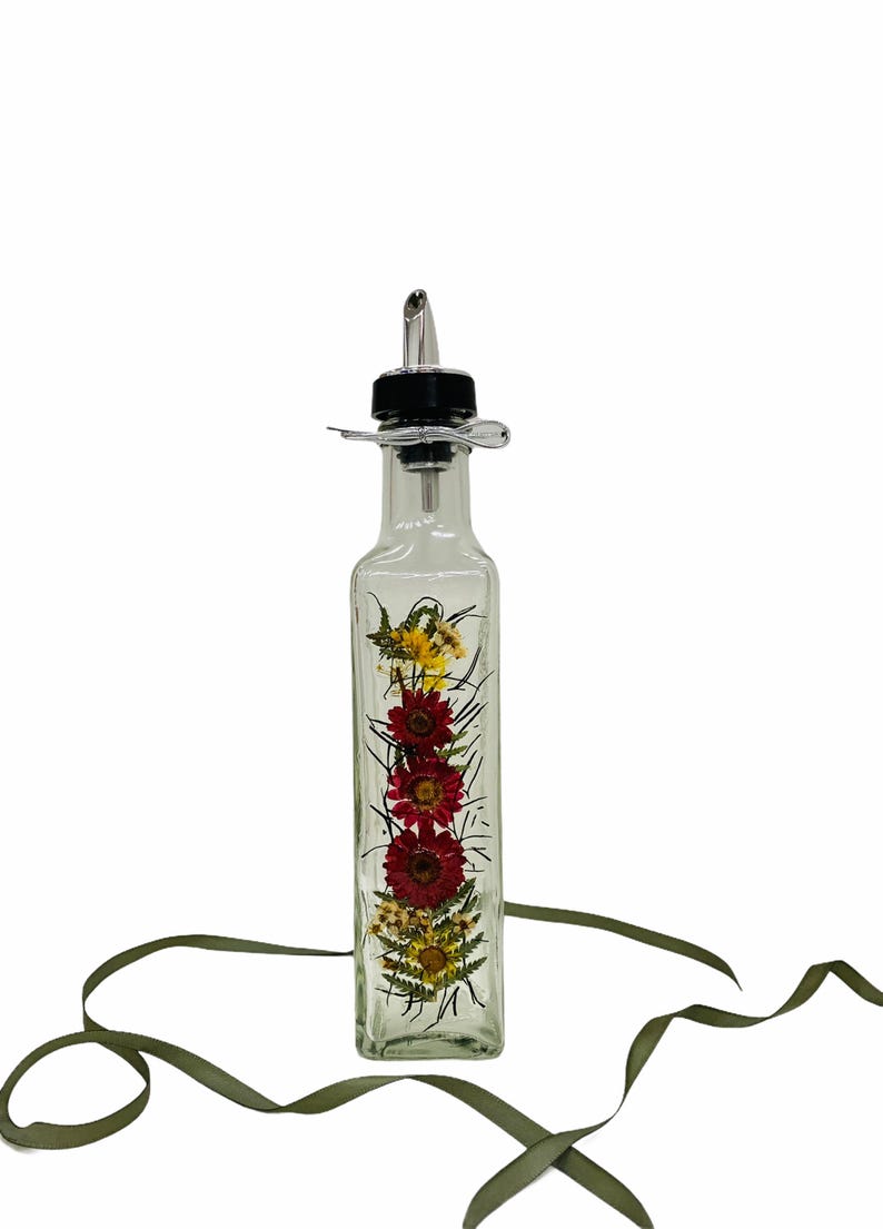 Puede incluir: Una botella de vidrio transparente con un pico de vertido negro y plateado. La botella est&aacute; llena de flores secas, incluyendo rojas, amarillas y verdes.