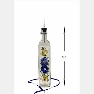 Puede incluir: Una botella de vidrio transparente con un pico de vertido de metal y un dise&ntilde;o floral con flores prensadas azules, amarillas y verdes. La botella mide 12,5 pulgadas de alto.