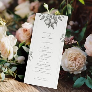 May include: A wedding program with a lemon and floral design, resting on a wooden surface. The program features the names Lyons Porter and Simon Cooper, along with the date, and a list of the ceremony events. Soft pink and white roses and greenery surround the program.