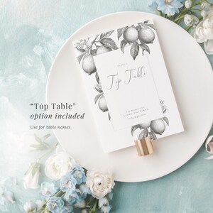Elegant top table sign included with monochrome lemon design. Use for table names. Shown in a holder laid on a plate, with a blue painted background and blue and white flowers