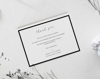 May include: A white thank you card with a black border and elegant script. The card includes the text "thank you" and a message of gratitude. An envelope and decorative elements are in the background.