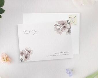 May include: A white thank you card with floral accents and the words "Thank You" in script. The card features a floral design in the upper right and lower left corners. A white envelope and a USA postage stamp are visible.