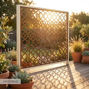 May include: A rectangular outdoor privacy screen featuring a brown metal panel with a repeating geometric lattice pattern, encased in a thick white frame. The screen stands upright on a wooden deck, casting intricate shadows in the sunlight.