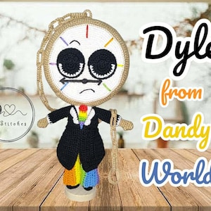 May include: A crochet doll featuring a round clock face with large black eyes, a tan border, and a black suit jacket over a rainbow-coloured tie and trousers. The doll has a tan crocheted chain attached to the head and side, with text reading Dyle from Dandy's World.