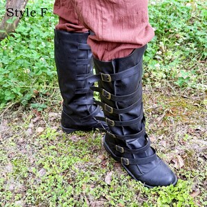 May include: Black leather knee-high boots with multiple straps and buckles. The boots have a flat sole. The text "Style F" is in the upper left corner. The boots are worn with reddish-brown trousers.