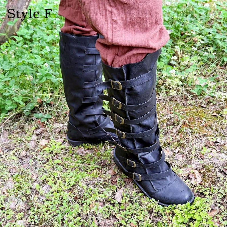 May include: Black leather knee-high boots with multiple straps and buckles. The boots have a flat sole. The text "Style F" is in the upper left corner. The boots are worn with reddish-brown trousers.
