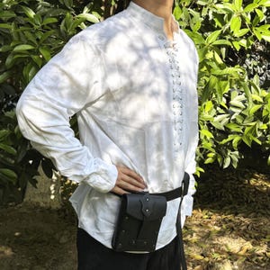 May include: A white long-sleeved shirt with a lace-up front and a black leather belt with a small pouch attached. The pouch has a flap with a metal buckle.