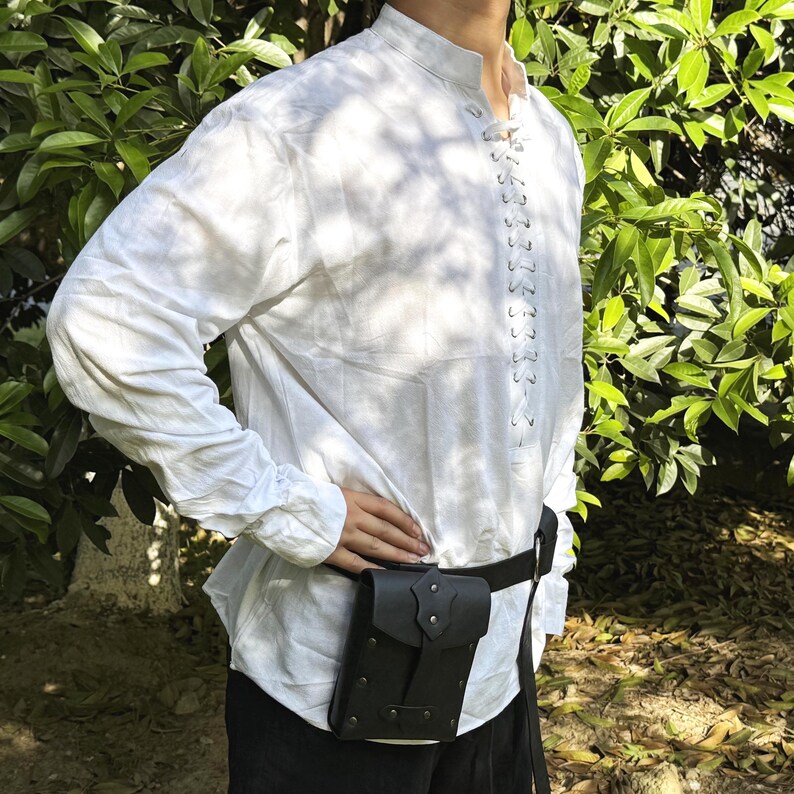 May include: A white long-sleeved shirt with a lace-up front and a black leather belt with a small pouch attached. The pouch has a flap with a metal buckle.