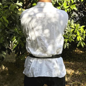 May include: A white long-sleeved shirt with a black belt. The shirt has a mandarin collar and is made of a lightweight fabric.